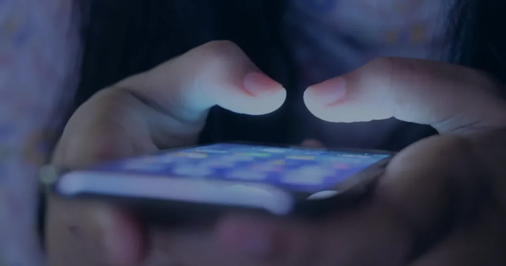 Mãos com smartphone na penumbra ilustrando os golpes mais comuns no WhatsApp
