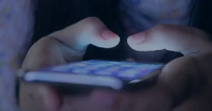 Mãos com smartphone na penumbra ilustrando os golpes mais comuns no WhatsApp